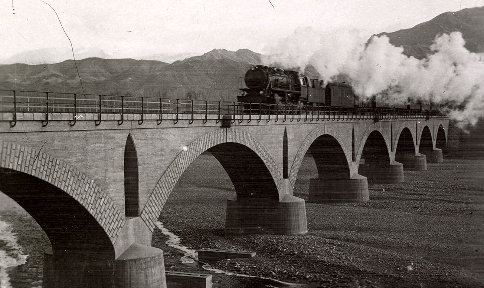 Arched bridge over a river with a steam train crossing atop